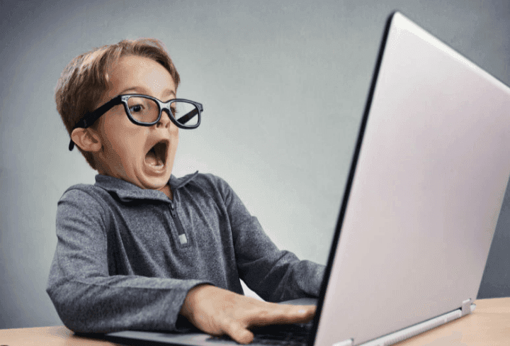 Person wearing glasses, sitting at a desk and using a large silver laptop.